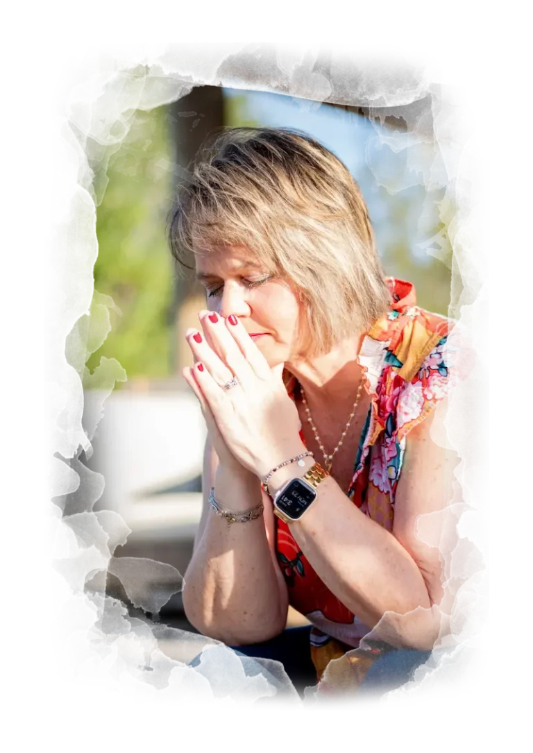 Kim Walker with short blonde hair sits with her hands clasped near her face, eyes closed, looking thoughtful or distressed. She wears a colorful top, a smartwatch, and has red nail polish. The background is blurred.